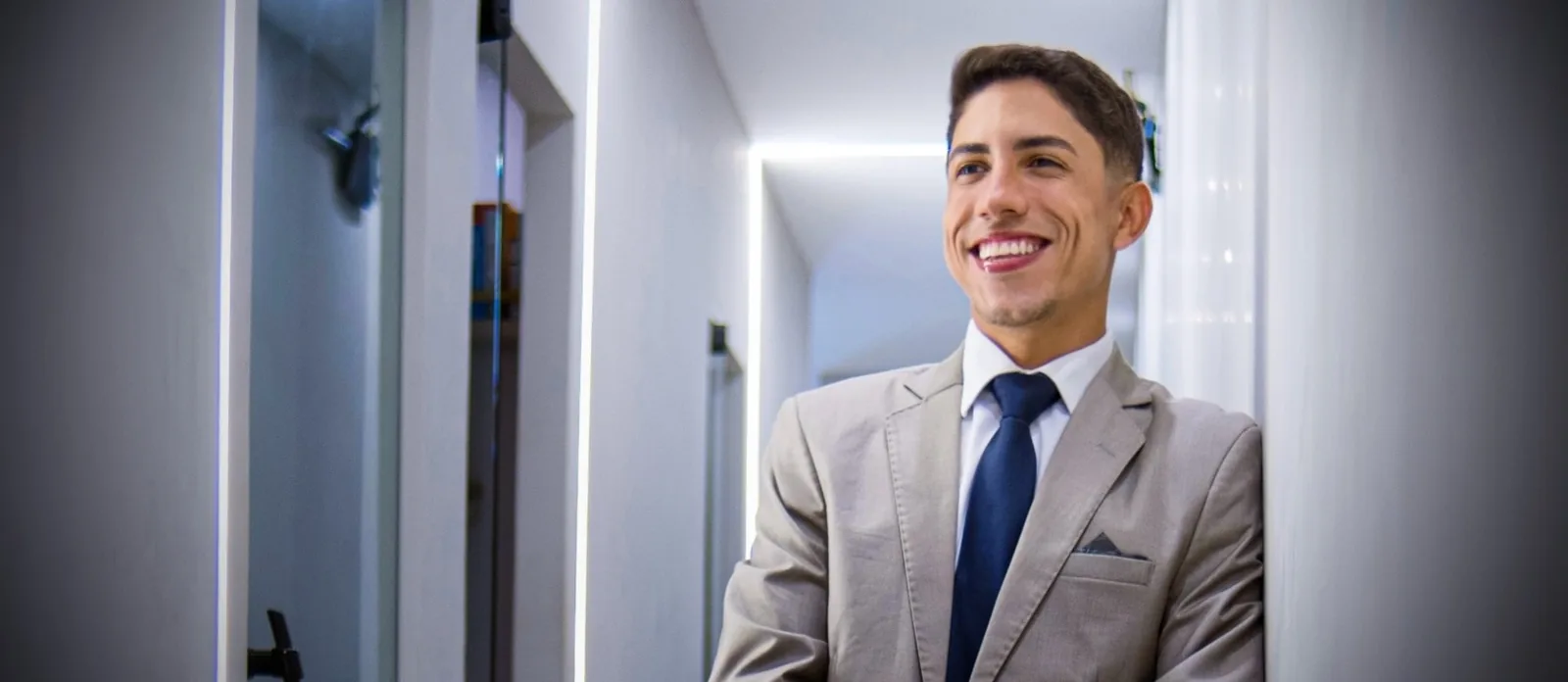 Alan Silva no corredor do escritório, de terno bege