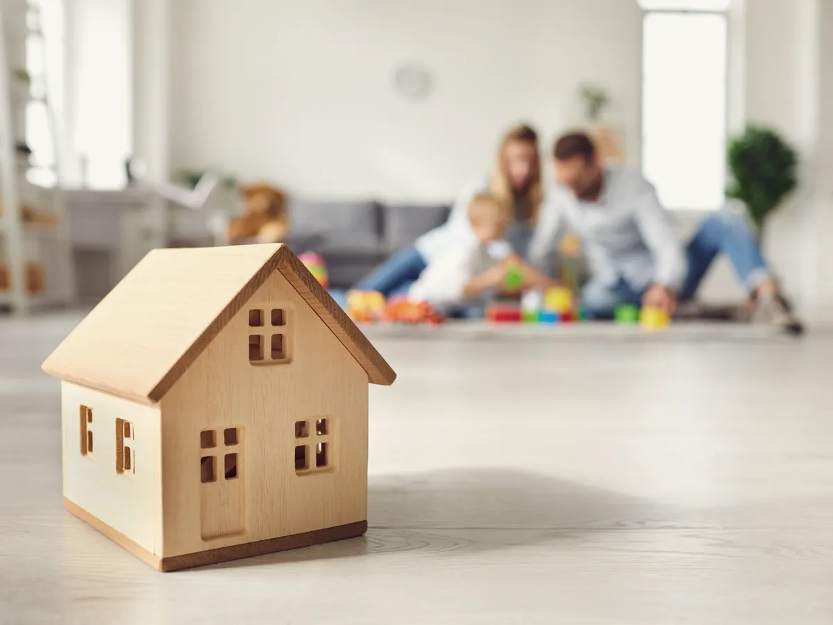 Casinha de madeira em primeiro plano e uma família brincando ao fundo